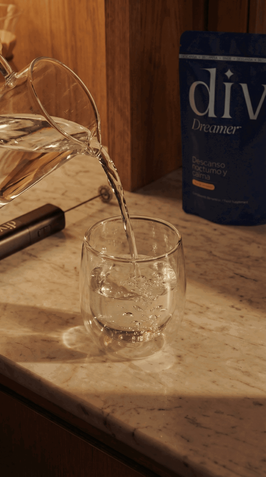 Agua vertiéndose desde una jarra de cristal en un vaso sobre una encimera de mármol, con la bolsa de Dive Dreamer detrás