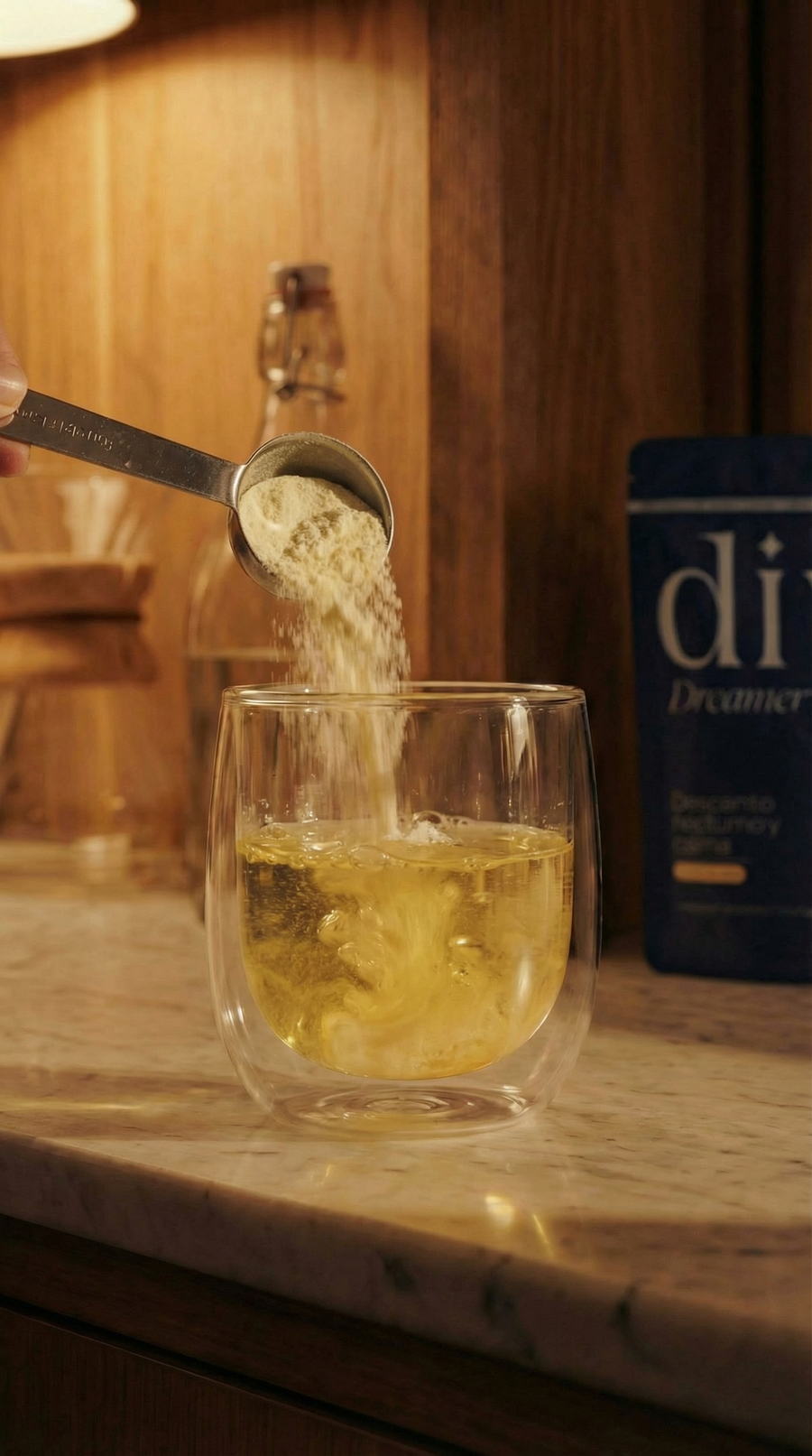 Cacito dosificador vertiendo el polvo de Dive Dreamer en un vaso de agua, con la bolsa del producto al fondo