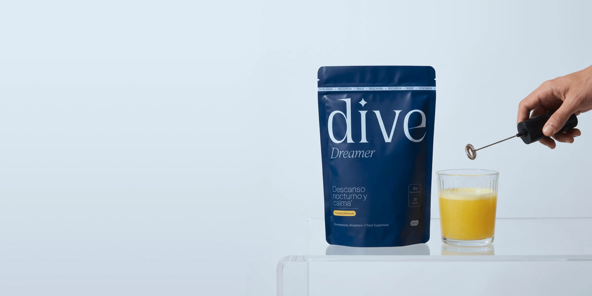 Bolsa de Dive Dreamer junto a un vaso de bebida amarilla que una mano mezcla con un espumador