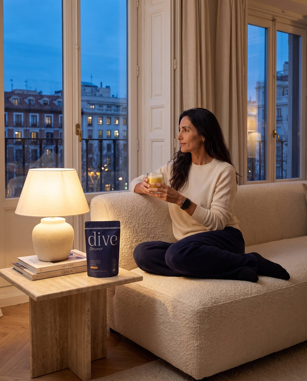 Mujer relajándose en el sofá por la noche con una bebida caliente junto a Dive Dreamer, suplemento natural para dormir mejor
