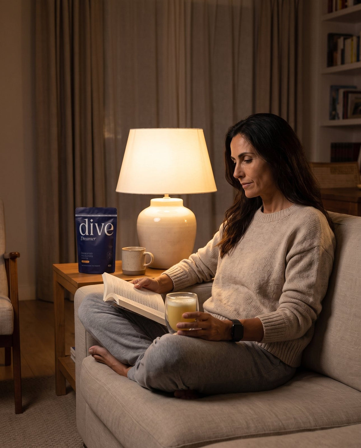 Mujer leyendo en el sofá junto a una lámpara con un vaso de Dive Dreamer